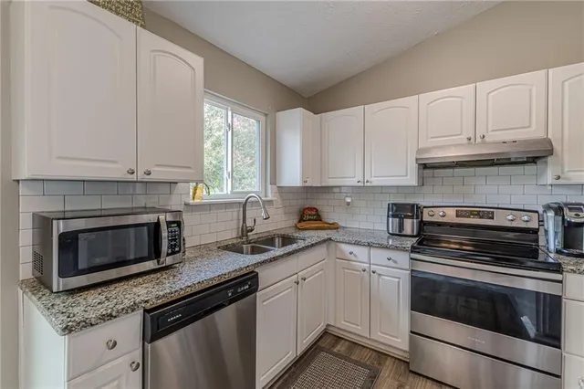a kitchen with granite countertop white cabinets stainless steel appliances and window