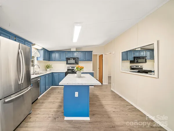 a kitchen with stainless steel appliances kitchen island granite countertop a refrigerator a stove top oven a sink dishwasher and white cabinets with wooden floor