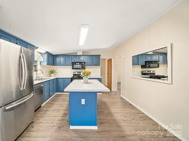 a kitchen with stainless steel appliances kitchen island granite countertop a refrigerator a stove top oven a sink dishwasher and white cabinets with wooden floor