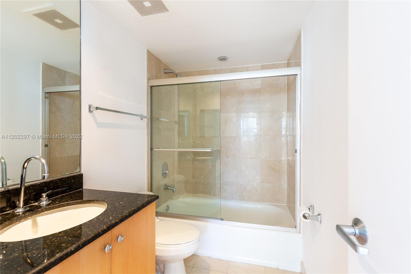 a bathroom with a granite countertop bathtub shower sink mirror vanity and toilet
