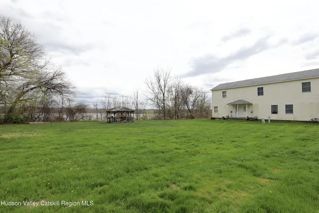 a view of a white house in front of a big yard with plants and large trees