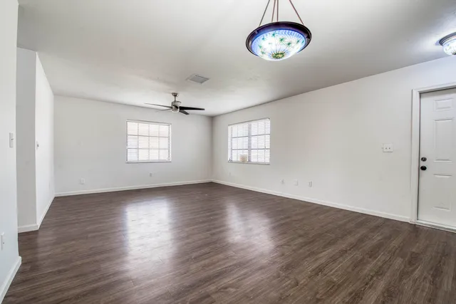 an empty room with wooden floor chandelier fan and windows