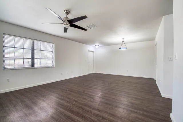 an empty room with wooden floor fan and windows