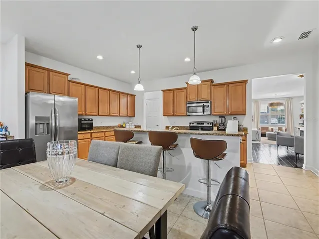 a kitchen with stainless steel appliances kitchen island granite countertop a refrigerator a stove a kitchen island a dining table and chairs