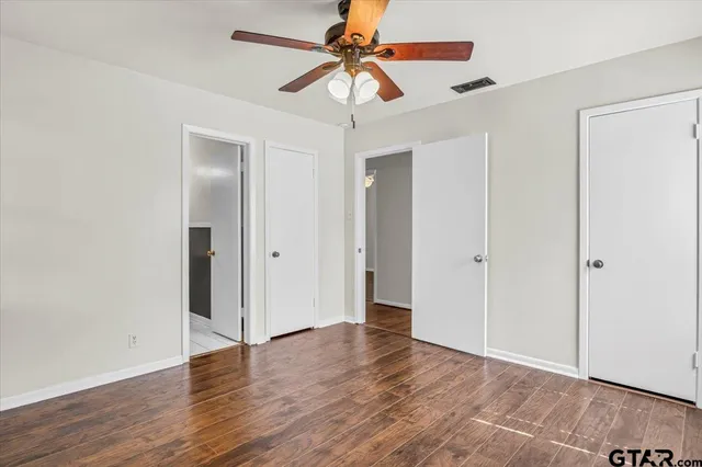 a view of an empty room with window a ceiling fan and wooden floor