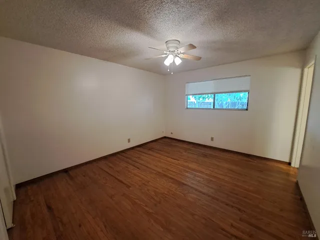an empty room with wooden floor chandelier fan and windows