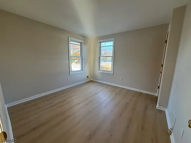 a view of an empty room with wooden floor and window