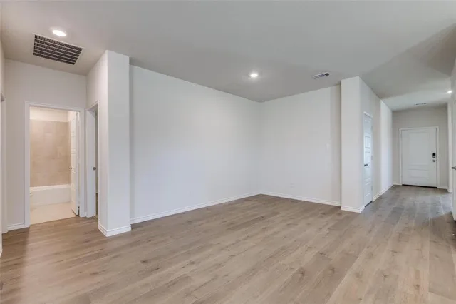 a view of an empty room with wooden floor and a bathroom