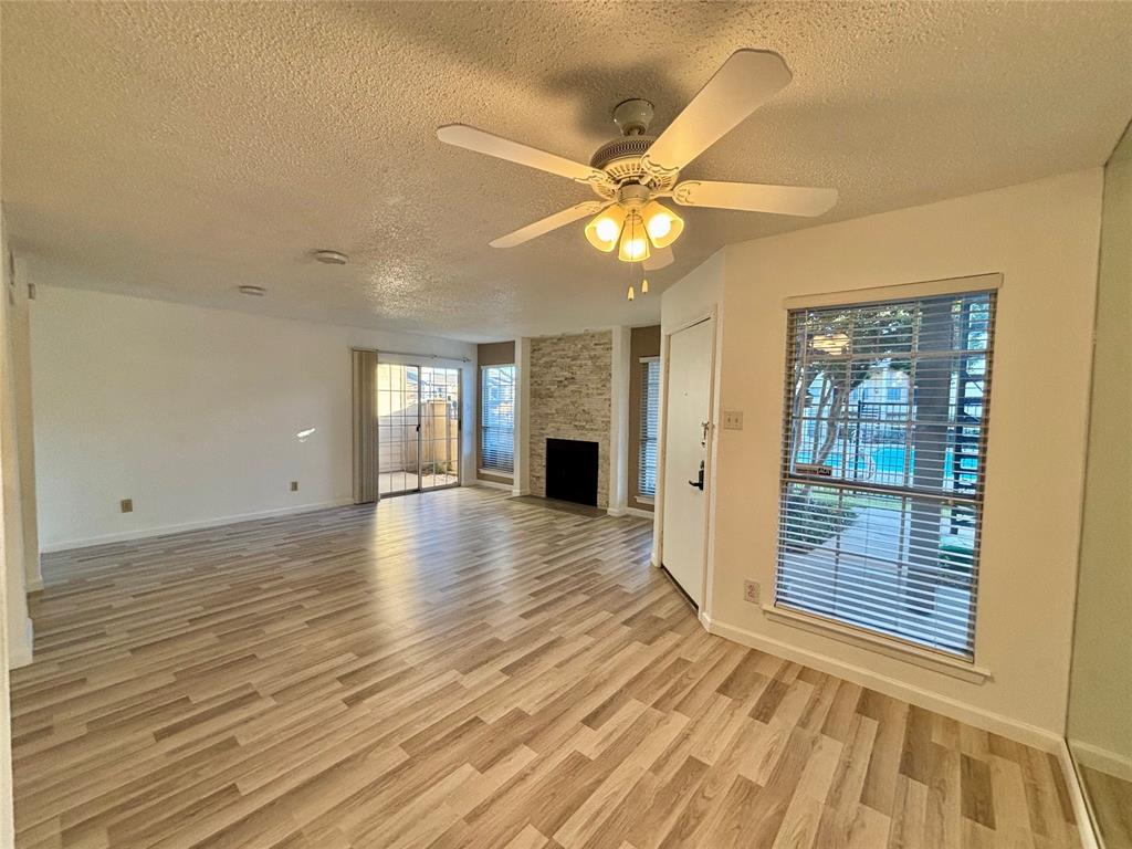 12480 Abrams Road, Unit 2805 Dallas, TX 75243 - Photo 4 of 18 Unfurnished living room featuring a textured ceiling, light wood-type flooring, a fireplace, and a ceiling fan
