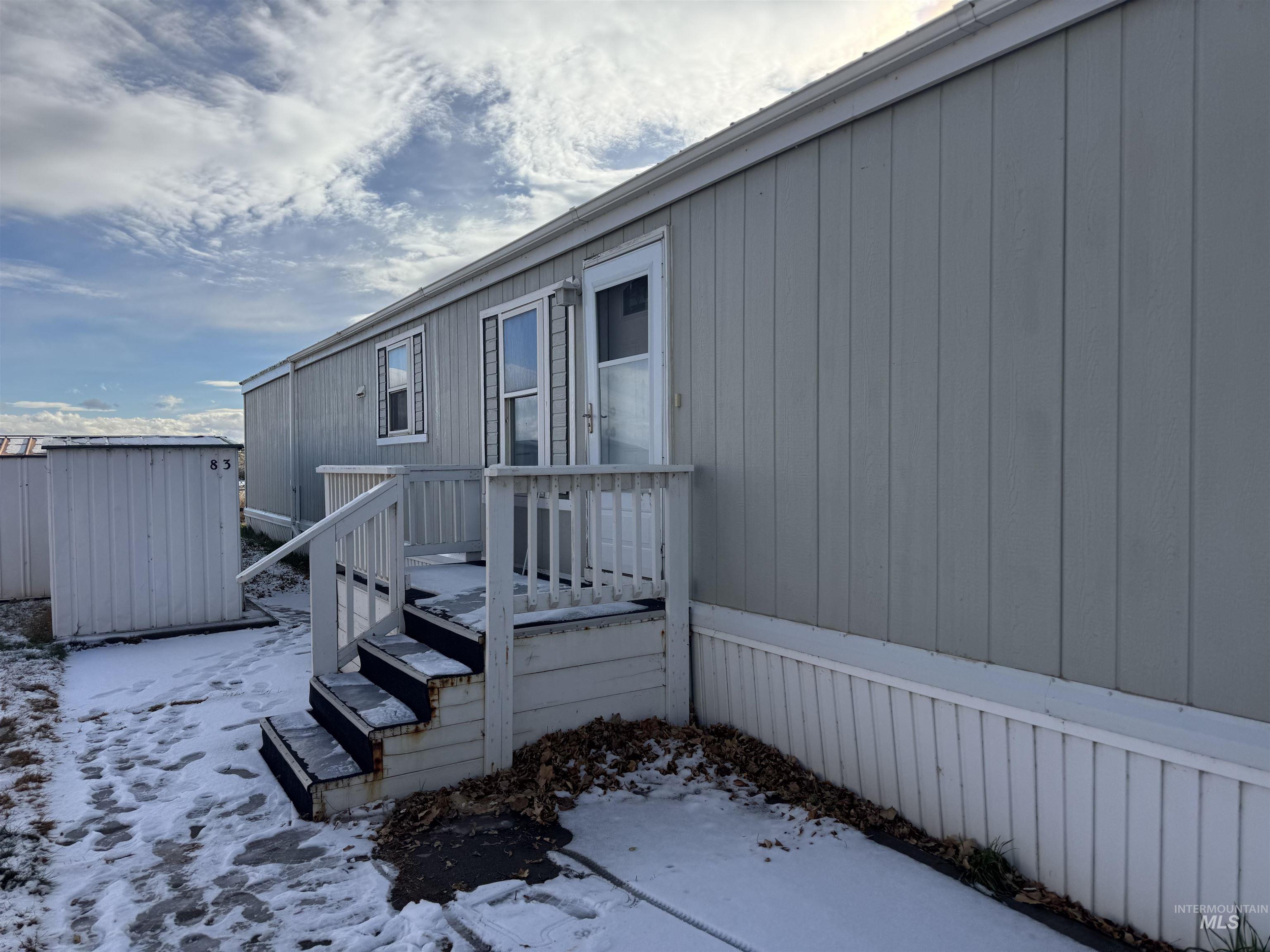 View of snow covered exterior featuring a wooden deck and a storage shed