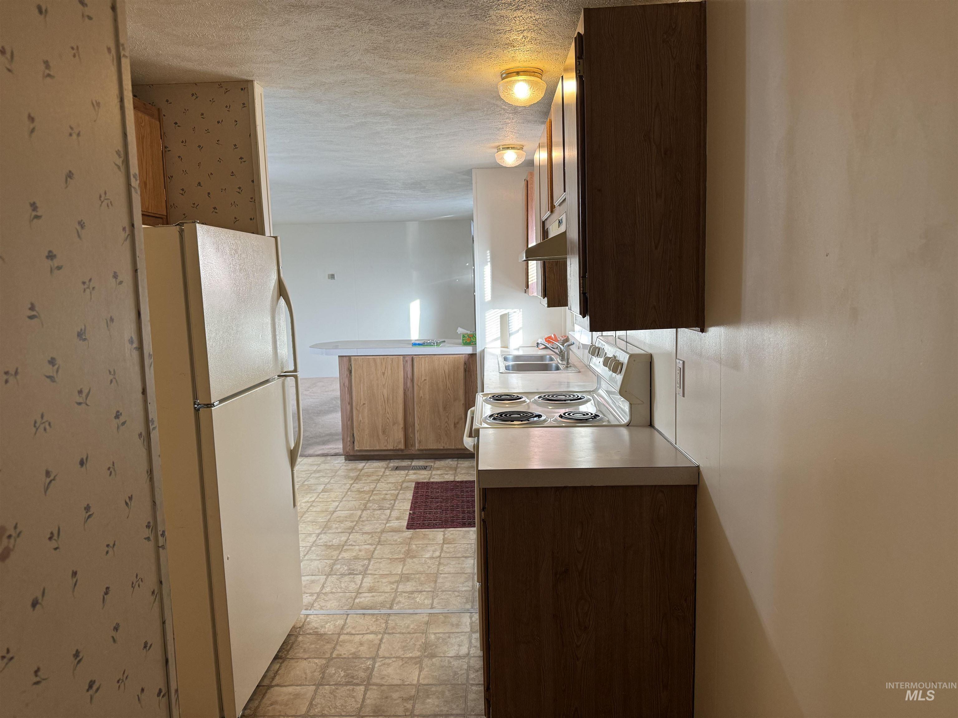 198 South Hills Road, Unit 83 Twin Falls, ID 83301 - Photo 11 of 21 Kitchen with freestanding refrigerator, a textured ceiling, light countertops, a peninsula, and under cabinet range hood