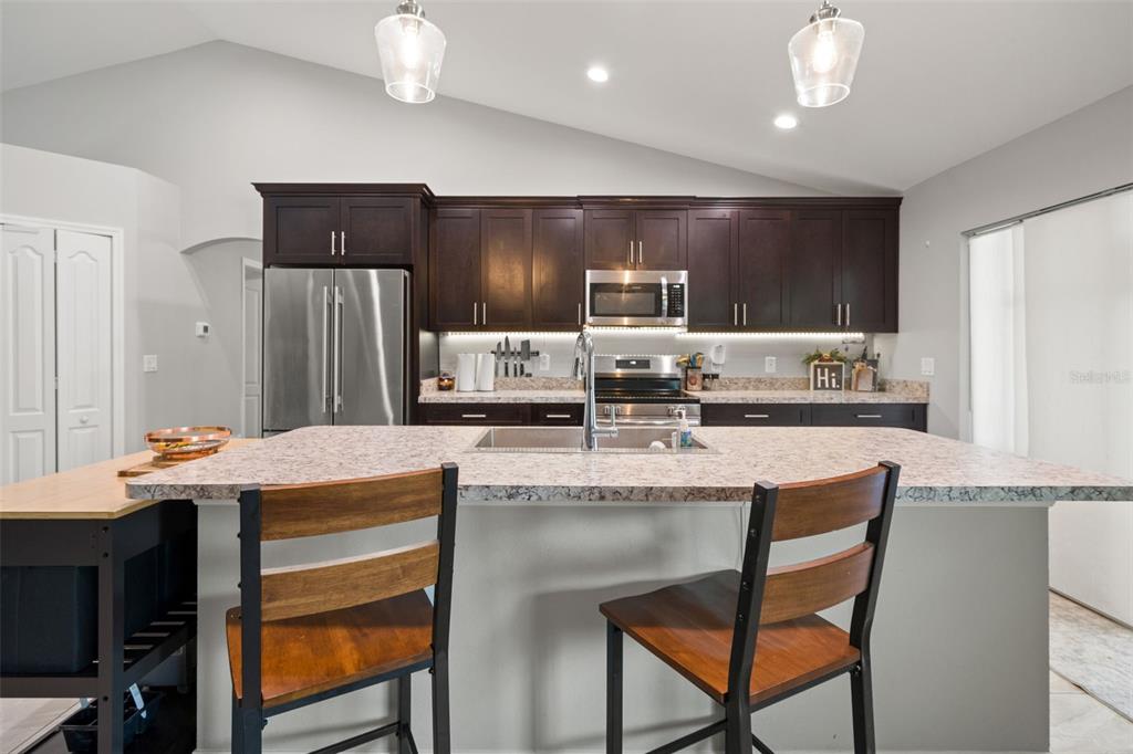 12015 Phoenix Avenue Weeki Wachee, FL 34614 - Photo 11 of 39 a kitchen with stainless steel appliances kitchen island granite countertop a dining table chairs and a refrigerator