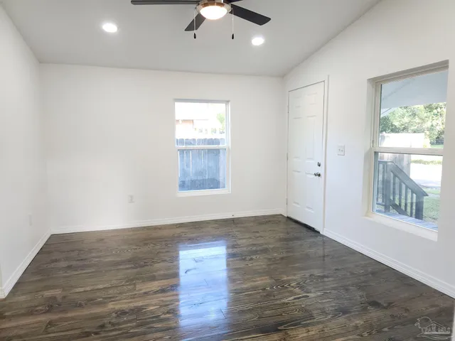 an empty room with wooden floor chandelier fan and windows