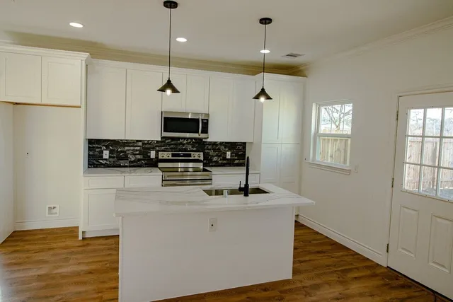 a kitchen with stainless steel appliances granite countertop a sink a stove a refrigerator and white cabinets