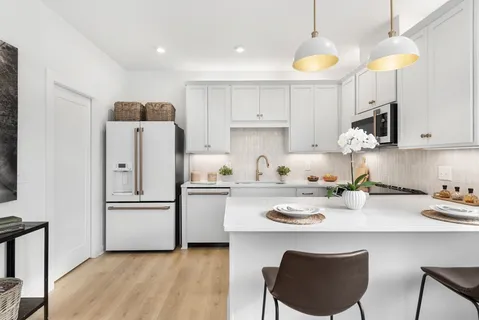 a kitchen with stainless steel appliances granite countertop a refrigerator a sink dishwasher a stove a dining table and chairs with wooden floor