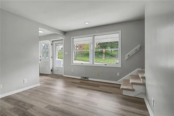 a view of an empty room with wooden floor and a window