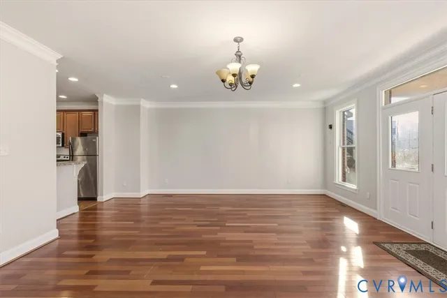 a view of an empty room with wooden floor and a kitchen