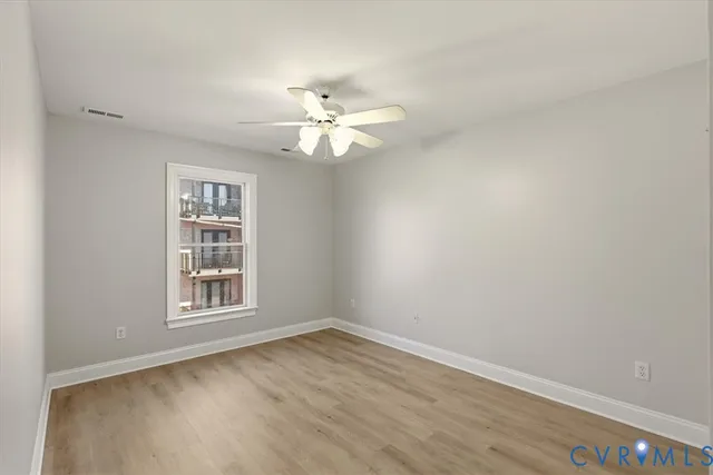 an empty room with wooden floor ceiling fan and window