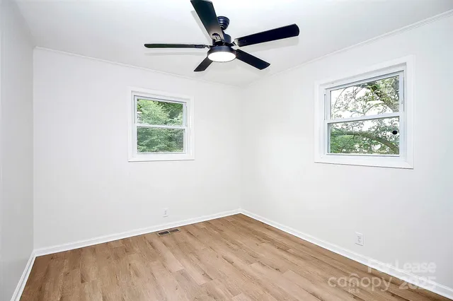 an empty room with wooden floor ceiling fan and window
