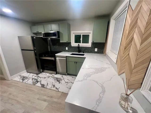 a living room with stainless steel appliances furniture a rug and a kitchen view