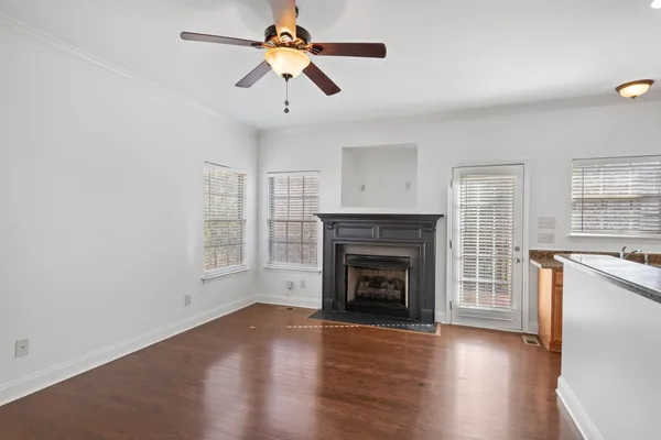 an empty room with wooden floor a ceiling fan a fireplace and windows