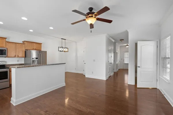 a view of an empty room and kitchen with wooden floor