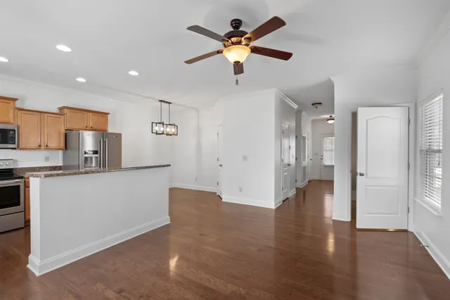 a view of an empty room and kitchen with wooden floor