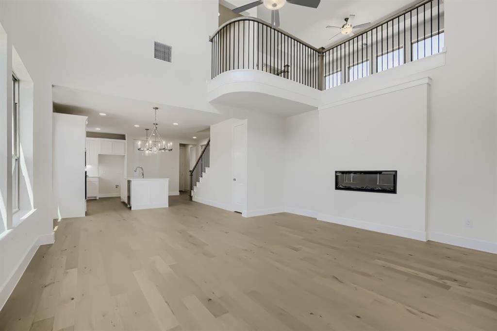 828 Stone Grv Road Lavon, TX 75166 - Photo 2 of 27 Open-concept interior featuring light wood-finish flooring, a contemporary fireplace, a kitchen island with a sink and chandelier, a staircase with dark railings, and a second-story balcony with dark balusters