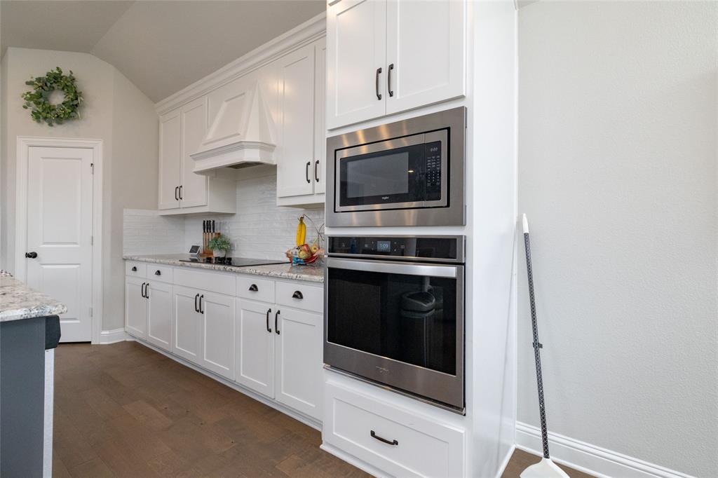4045 Grove Valley Road Midlothian, TX 76065 - Photo 16 of 34 Kitchen with stainless steel appliances, white cabinetry, dark wood-style floors, light stone countertops, and vaulted ceiling