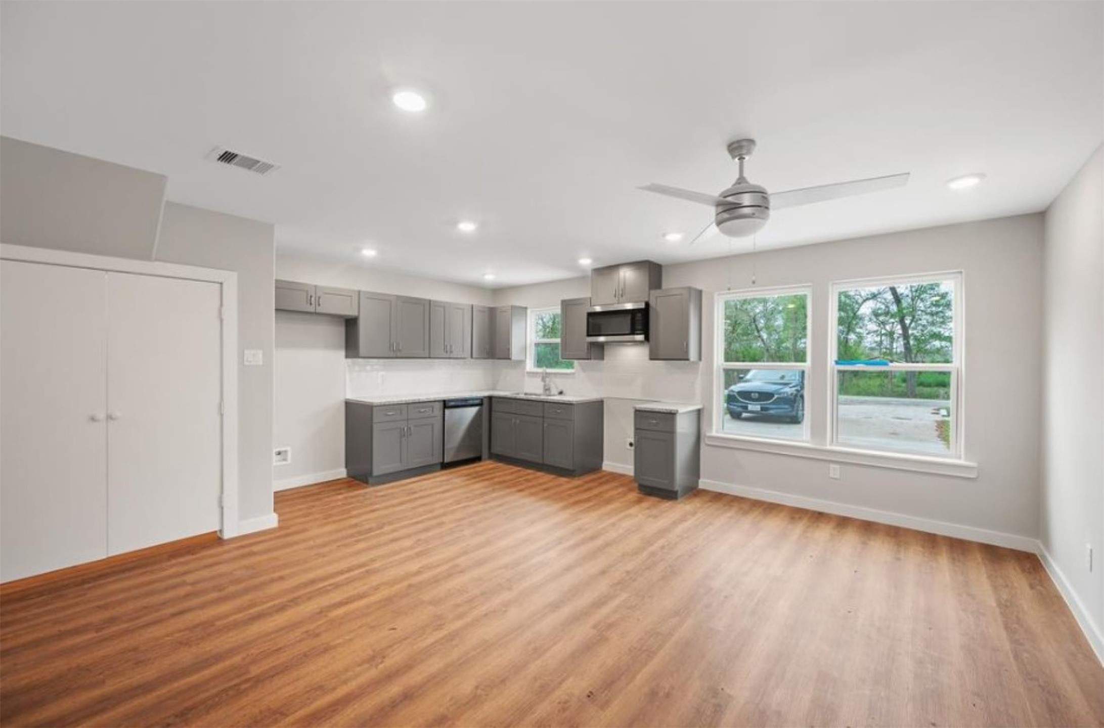 8217 Crestview Drive Houston, TX 77028 - Photo 4 of 25 This is a bright, modern kitchen with gray cabinets, stainless steel appliances, and hardwood flooring. It features ample natural light from large windows and is equipped with recessed lighting and a ceiling fan.