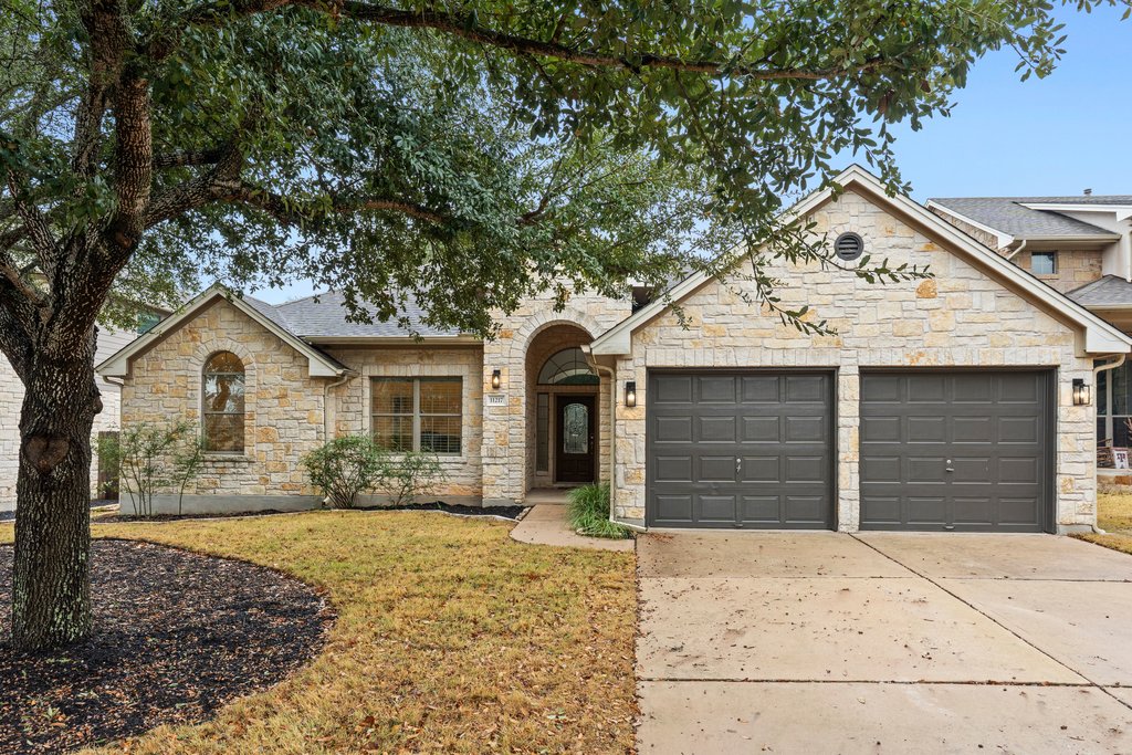 French provincial home with stone siding, concrete driveway, a garage, and a front lawn
