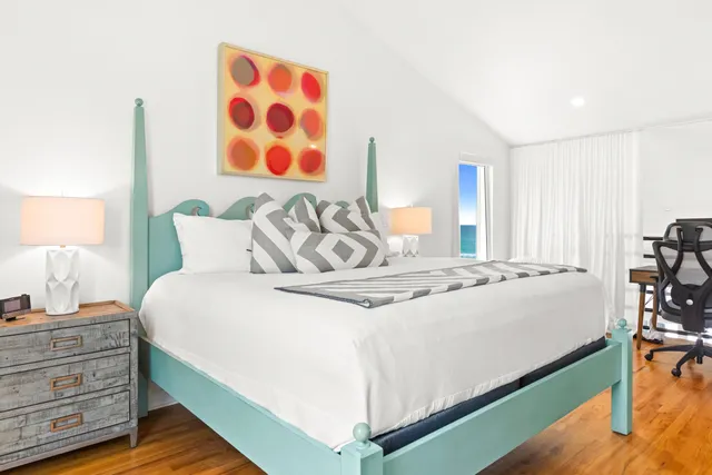 a bedroom with a bed and a lamp on dresser with wooden floor