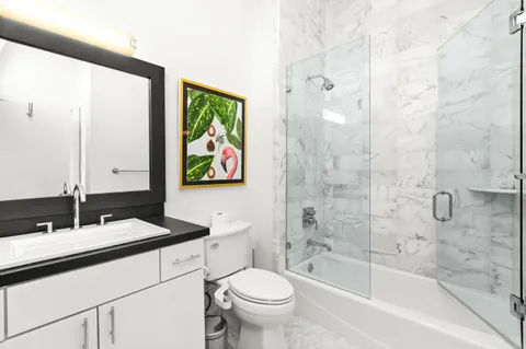 a bathroom with a granite countertop sink a toilet a mirror a bathtub and shower