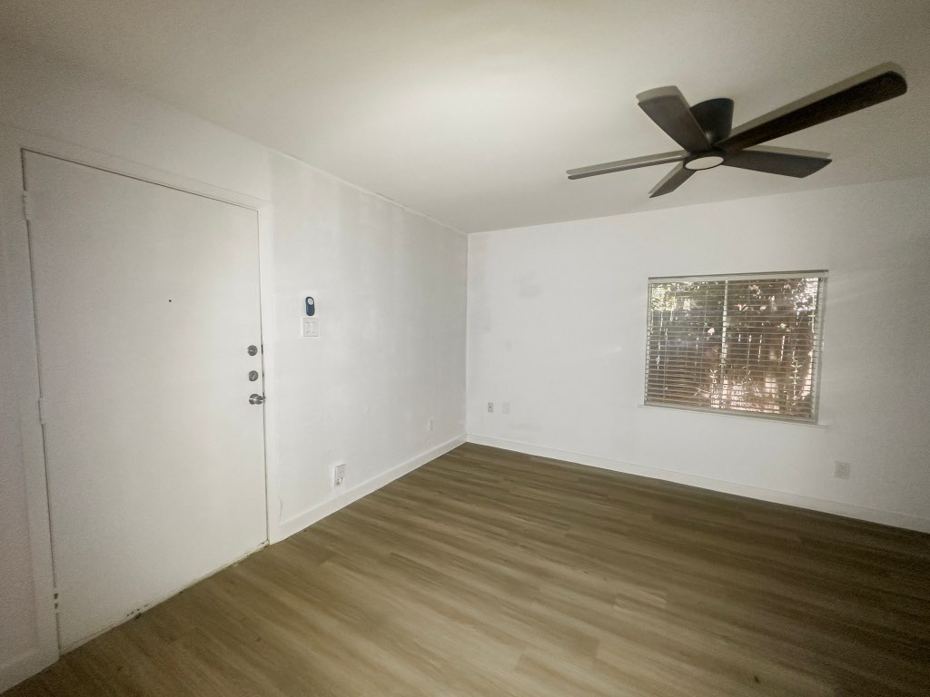 a view of an empty room with wooden floor and a ceiling fan