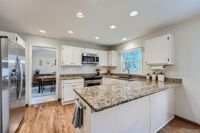 a kitchen with stainless steel appliances granite countertop a stove top oven a sink dishwasher and a refrigerator with wooden floor