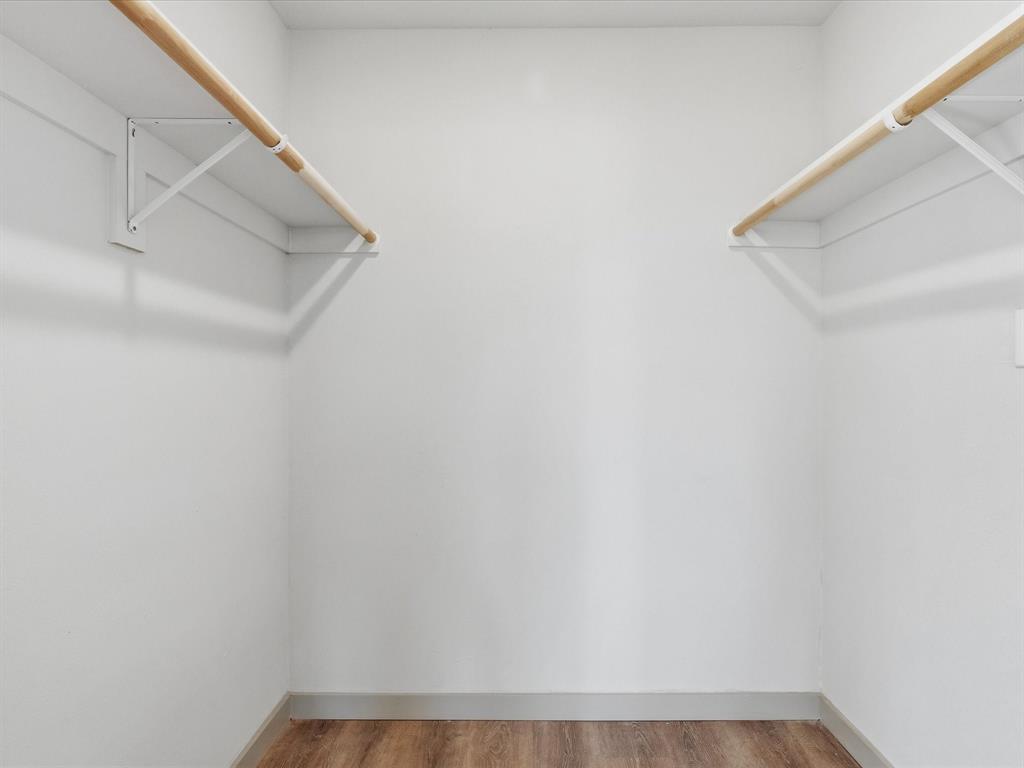 289 County Road 4655 Rhome, TX 76078 - Photo 16 of 34 Second Bedroom Walk-in Closet Neutral white walls with wood-finish flooring, featuring two wooden hanging rods and white shelving