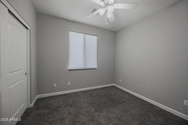 an empty room with a chandelier fan and windows