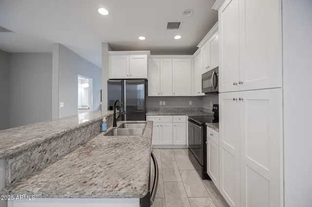 a kitchen with kitchen island granite countertop a stove a sink dishwasher a refrigerator and white cabinets with wooden floor