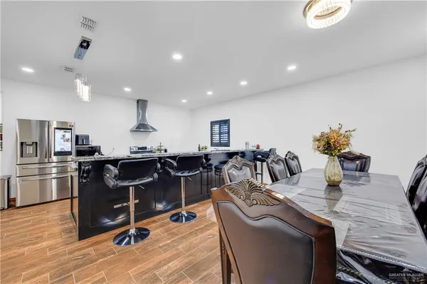 a living room with stainless steel appliances kitchen island granite countertop a table chairs and a refrigerator