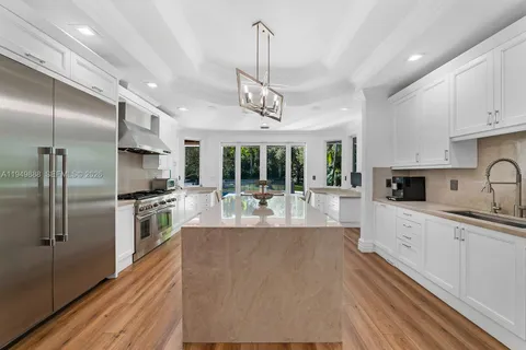 a large kitchen with stainless steel appliances kitchen island granite countertop a refrigerator a sink dishwasher a stove and white cabinets with wooden floor