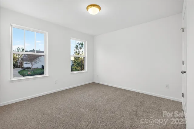 an empty room with windows and view of kitchen