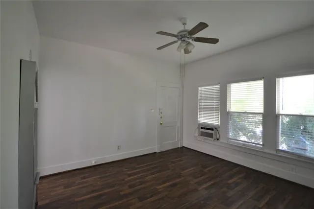 an empty room with wooden floor fan and windows