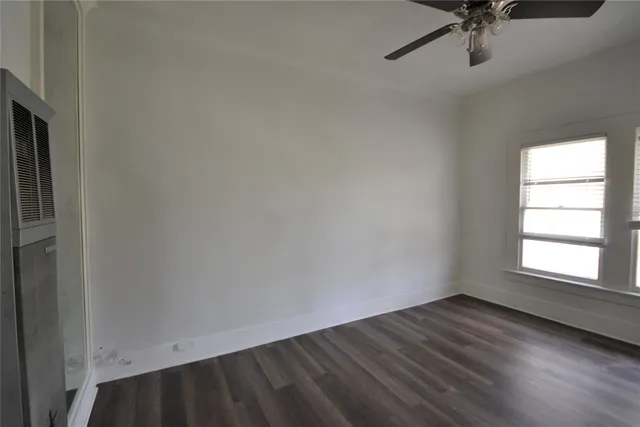 an empty room with wooden floor fan and windows