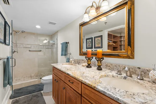 a bathroom with a granite countertop double vanity sink mirror double shower and a toilet