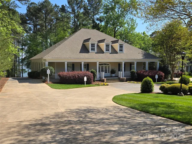 a view of a white house with a big yard plants and large trees