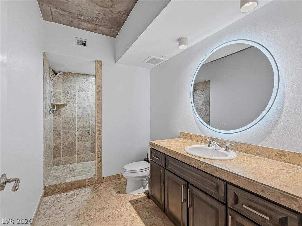 360 East Desert Inn Road, Unit 607 Las Vegas, NV 89109 - Photo 33 of 55 A well-appointed bath features a spacious tiled shower and an illuminated circular vanity mirror.