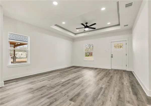 an empty room with wooden floor chandelier fan and windows