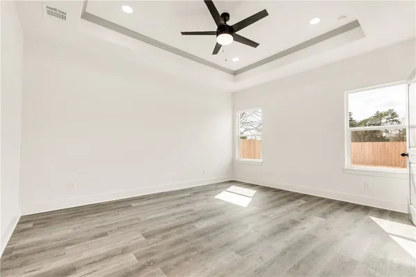 an empty room with wooden floor fan and windows