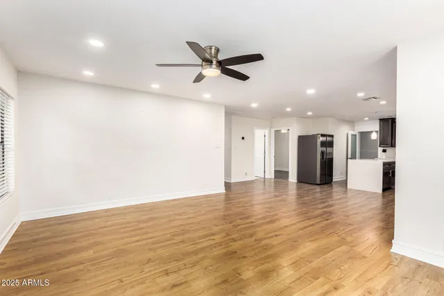 a view of an empty room with wooden floor and a ceiling fan