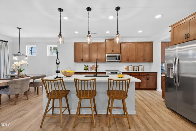 a kitchen with stainless steel appliances granite countertop a stove a refrigerator a kitchen island a dining table and chairs with wooden floor